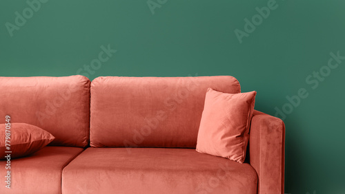 Close up of coral comfortable couch with cushions against green wall