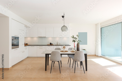 Large modern white kitchen with a marble table and four chairs in front. This is the interior of a modern flat.