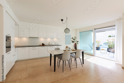 Large kitchen with dining table inside. Modern space and a window opening onto a terrace.