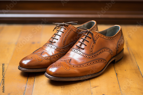 A pair of classic brown leather brogues with punched detailing on a vintage wooden floor.
