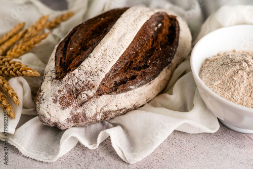 On a gray background, rye bread, ears of corn and flour in a plate.