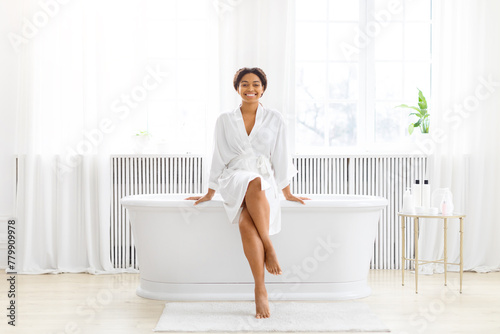 Woman in bathrobe sitting on tub at home