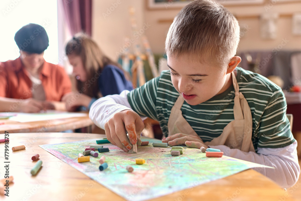 Fototapeta premium Close up portrait of young boy with Down syndrome drawing picture and smiling during art therapy class