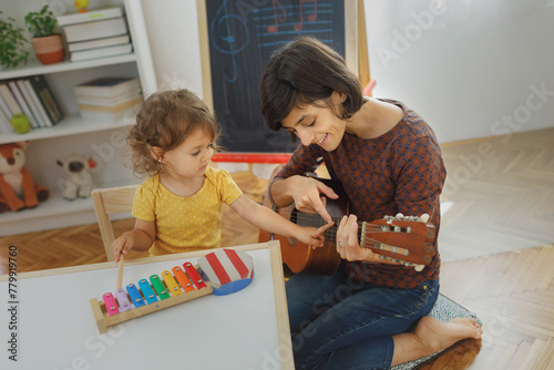 Mother and child playing with music instruments at home. Mother learning kid to play guitar. 