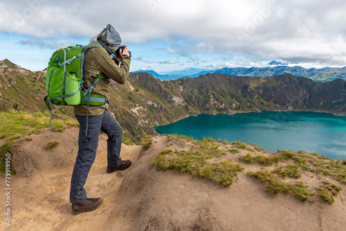 Male photographer in trekking outfit taking photographs of the Quilotoa Lagoon along the Quilotoa Loop Hike, Andes Mountains, Quito, Ecuador.