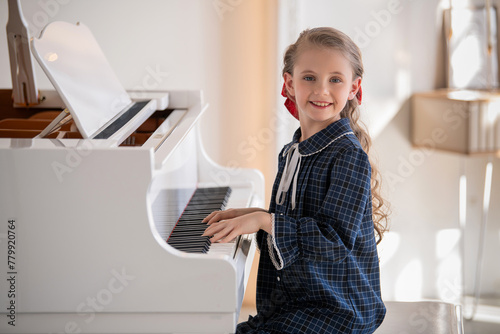A little girl plays a big white piano in a bright sunny room