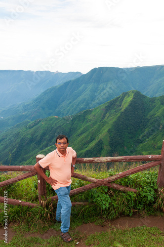 A tourist is standing beside railings at perched atop the East Khasi Hills, the Laitlum Canyons that extend over deep valleys, steep cliffs. Hiking retreat offering trails through green meadows. photo