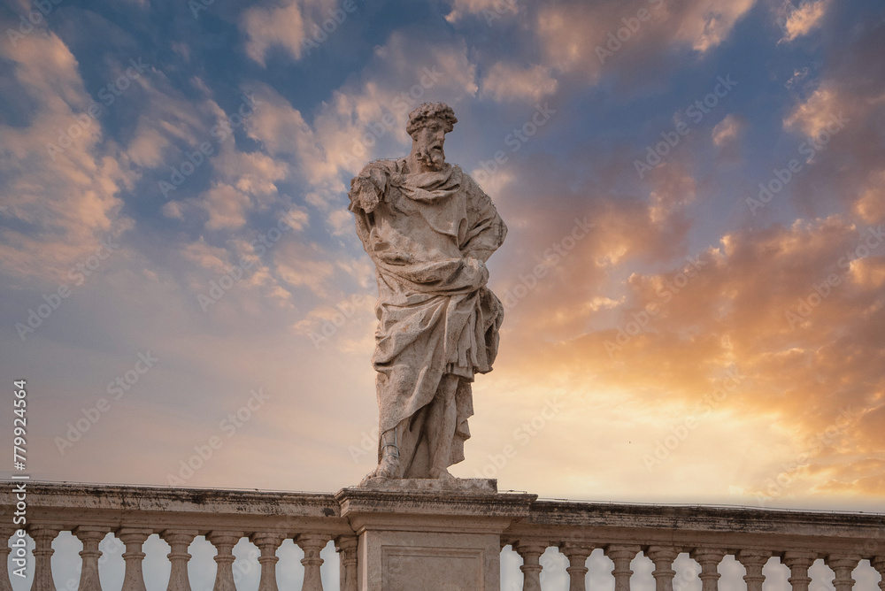Classical marble statue against dramatic sunset sky, with contemplative male figure donning laurel wreath, placed on pedestal in Vatican location, framed by elegant balustrade.