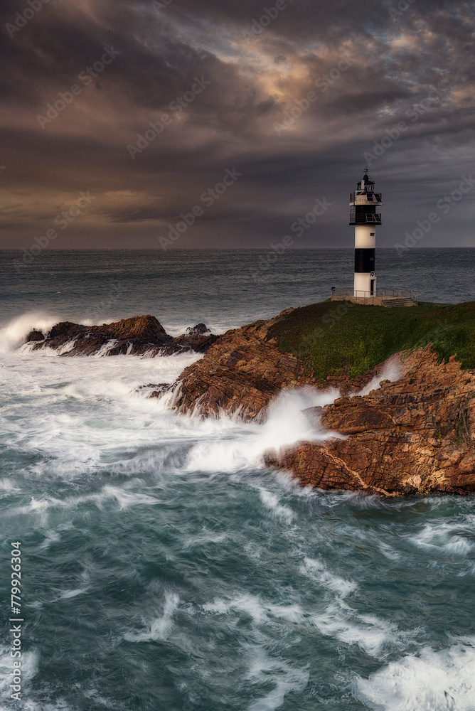 Pancha Island Lighthouse in Ribadeo, Lugo, Galicia, on a sunset with many clouds and a dramatic sky with the waves breaking strongly against the coast