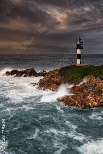 Pancha Island Lighthouse in Ribadeo, Lugo, Galicia, on a sunset with many clouds and a dramatic sky with the waves breaking strongly against the coast