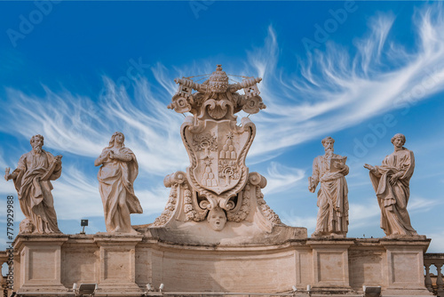 Statues with ornate coat of arms under a dramatic sky in Vatican City. Classical sculptures and symbolic imagery provide historical and religious significance.