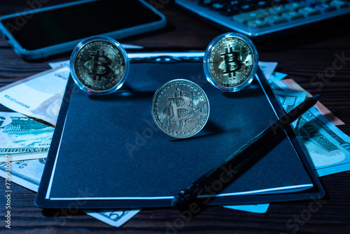 Several bitcoin coins on a black sheet. Black notepad and black pencil.