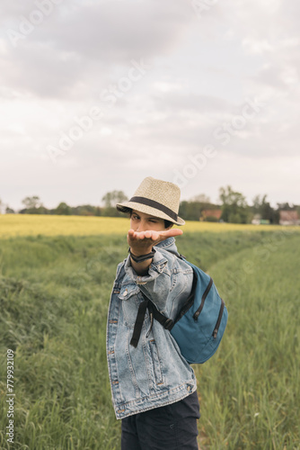 Teenage girl with straw hat and denim jacket makes a hand gesture while hiking in the field