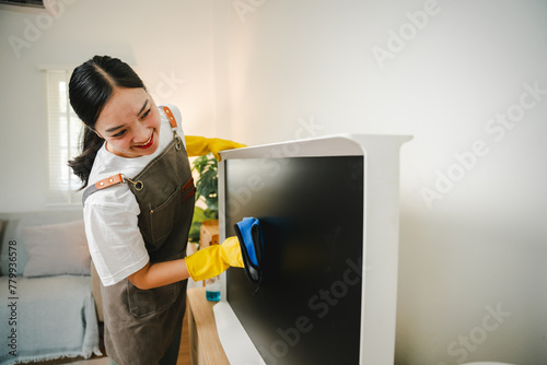 Young housewife is wiping dust off the TV with a microfiber cloth in the living room. Housekeeping concept