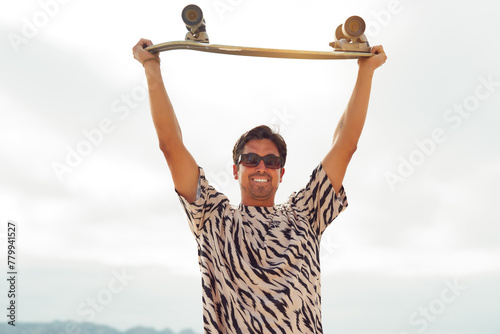 portrait handsome latin guy holding a skateboard over his head outdoors on the beach 