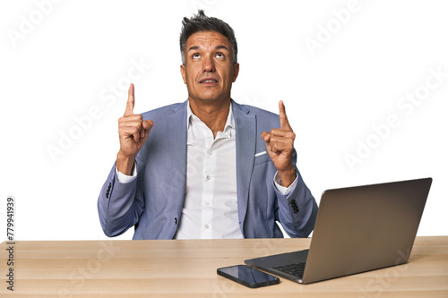 Elegant businessman at desk with laptop pointing upside with opened mouth.