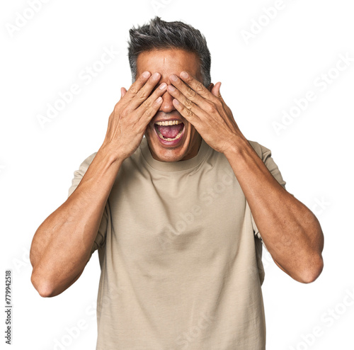 Middle-aged Latino man covers eyes with hands, smiles broadly waiting for a surprise.