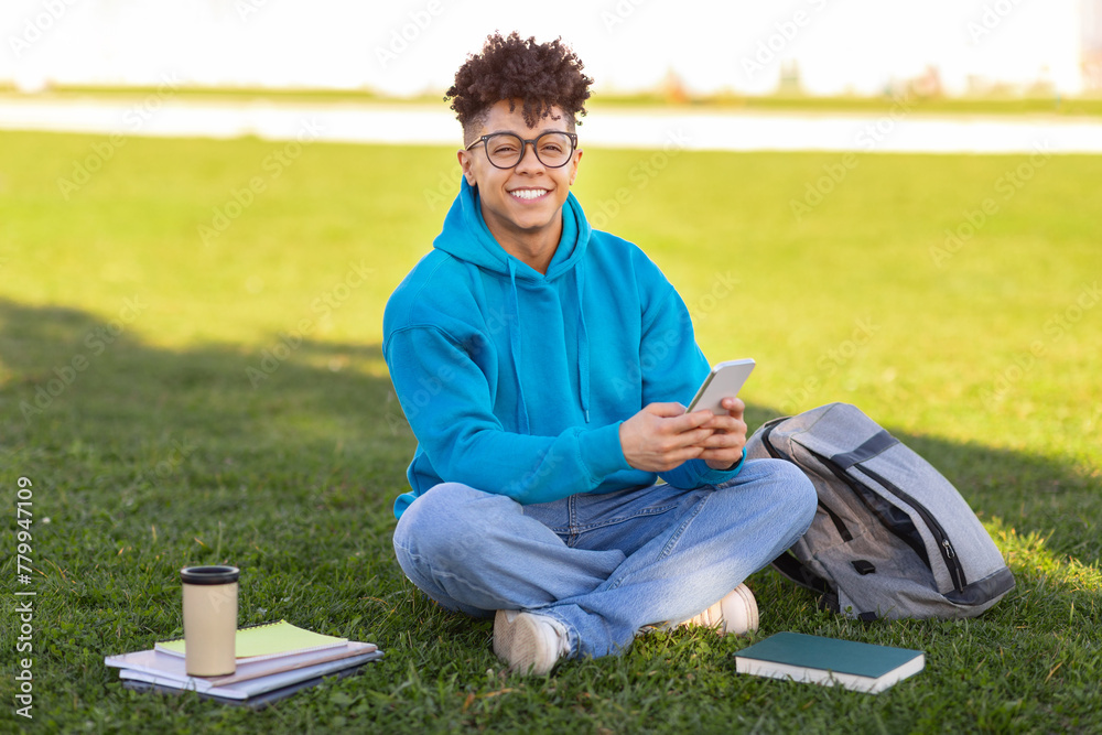 Fototapeta premium Student sitting on grass with smartphone, studying at park