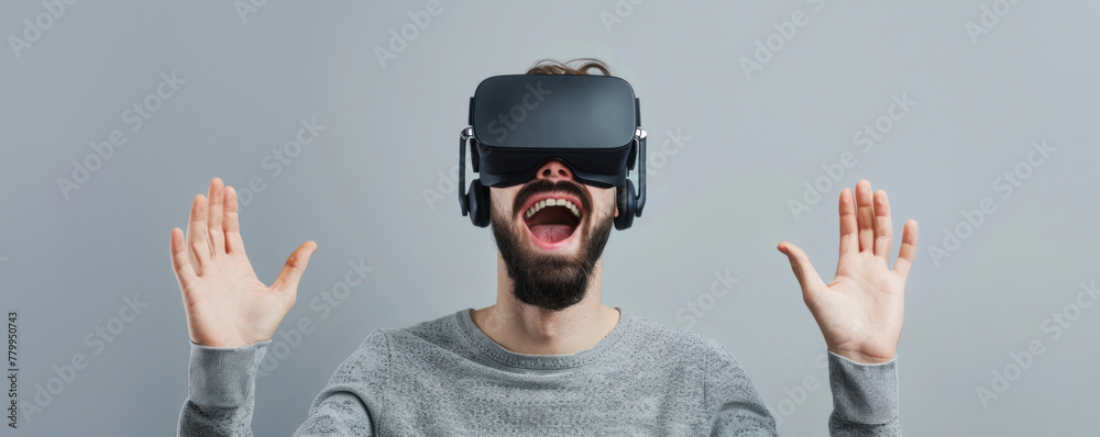 An ecstatic man experiencing virtual reality with hands raised, against a neutral backdrop, ideal for emphasizing the emotion of VR gaming or the impact of virtual training programs. An ecstatic man experiencing virtual reality with hands raised, against a neutral backdrop, ideal for emphasizing the emotion of VR gaming or the impact of virtual training programs.