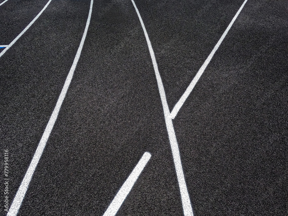 Track and Field Running Lanes. Overhead view of a rubber black running surface with white lane lines. There is a slight curve of the white lane lines. 