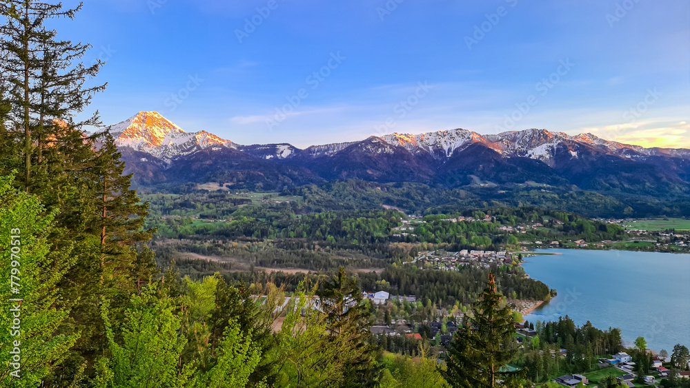Obraz premium Panoramic sunset view on Lake Faak from Taborhoehe in Carinthia, Austria, Europe. Surrounded by high Austrian Alps mountains. Water surface reflecting soft sunlight. Remote alpine landscape in summer