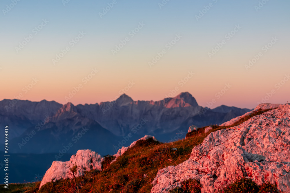 Selective close up view of rocks looking at sunset from Dobratsch on Julian Alps and Karawanks in Austria, Europe. Silhouette of endless mountain ranges with orange sky. Jagged sharp peaks and valleys