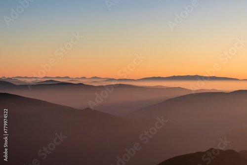Panoramic sunrise view from Dobratsch on High Tauern and Nocky Alps in Austria, Europe. Silhouette of endless mountain ranges covered by mystical fog in valley. Jagged sharp peaks and alpine landscape © Chris