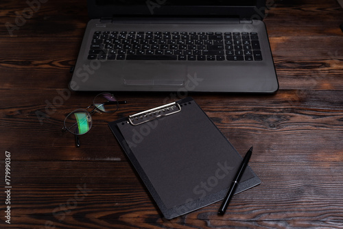 Black notepad on the table. Glasses and pen on the table. Desktop with laptop and notepad.