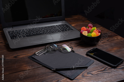 Desk in the office. Laptop and sweets on the table. Glasses and notepad on the surface.