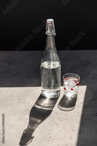 objects and drinks concept - bottle of water and glass with ice and cranberries on sunny floor