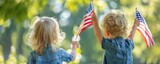 Two toddlers holding American flags in a garden. Rear view of children with patriotic symbols.