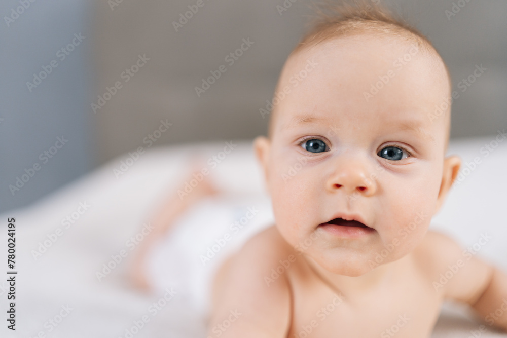 Closeup of cute newborn baby lying in bed trying to crawl waving hand at home. Front view of adorable little kid having good mood. Rising girl, first steps in crawling after hand plank. Closeup of cute newborn baby lying in bed trying to crawl waving hand at home. Front view of adorable little kid having good mood. Rising girl, first steps in crawling after hand plank.