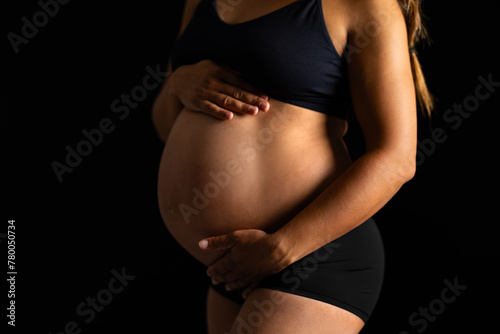 Pregnant Woman Embracing Her Belly in Dark Backdrop
