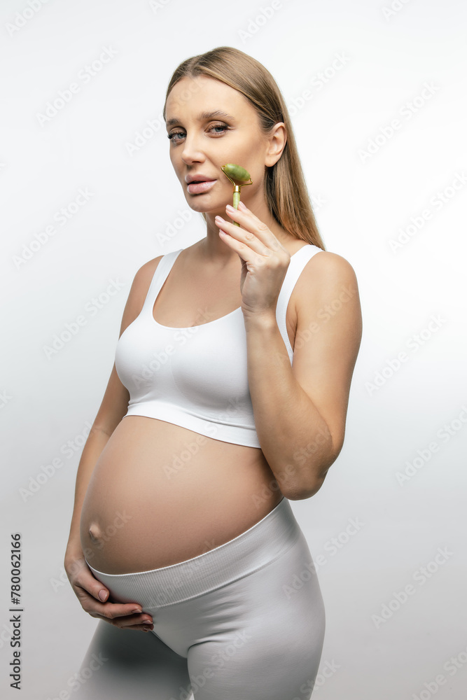Cute pregnant young woman massaging her face with roller