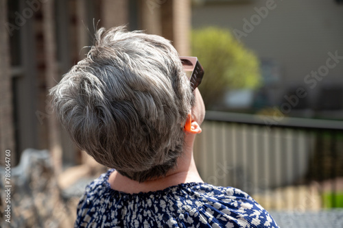 Older woman with graying hair shot from behind watching eclipse with glasses