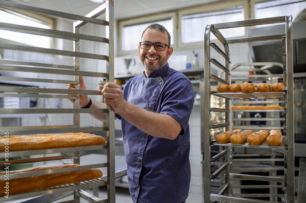 Professional man baker near fresh baked bread on tray rack trolley