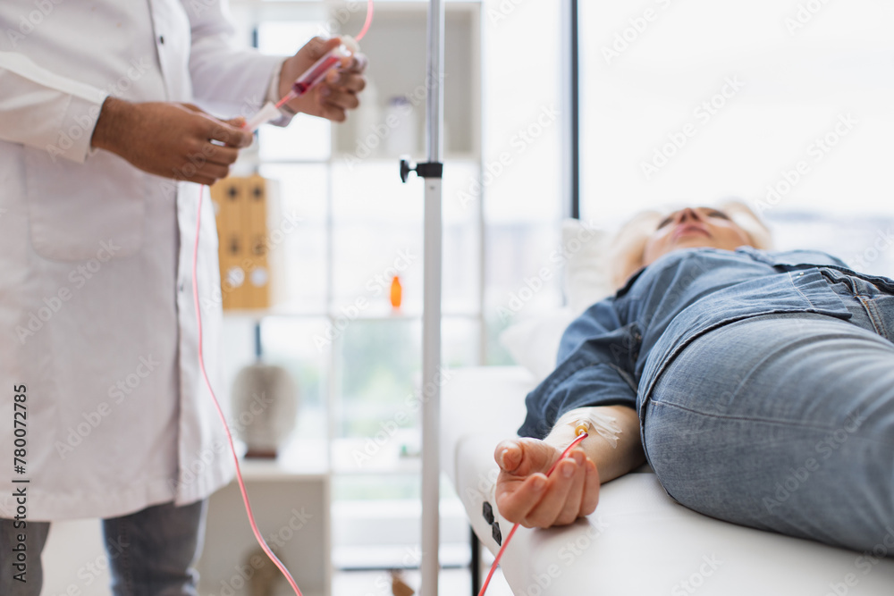 Obraz premium Cropped view of Caucasian senior woman making blood transfusions while young male making system review. Efficient general practitioner checking tubes which blood flows of female lying on exam couch.