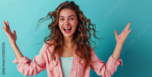 A woman with long hair is smiling and waving her arms in the air. Photo of excited cheerful woman wear shirt smiling open mouth rising arms palms isolated blue color background © Nataliia_Trushchenko