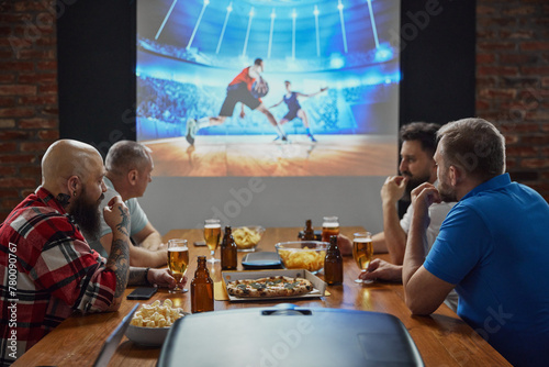 Men, friends gathering to watch online basketball match with enthusiasm translation on TV, drinking beer and eating snacks. Concept of sport, championship, game, sport fans, leisure