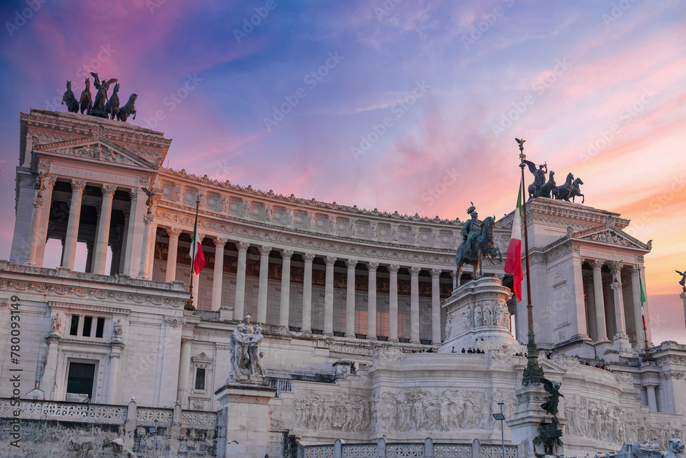 Neoclassical Altare della Patria monument in Rome, Italy. White marble structure with columns, sculptures, and Italian flags. Statue of Victor Emmanuel II on horseback on top.