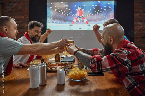 Fototapeta Naklejka Na Ścianę i Meble -  Sports enthusiasts, friends gathering at home to watch online hockey game on TV, with beer and snacks amplifying the excitement. Concept of sport, championship, game, sport fans, leisure