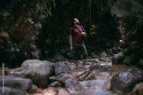 A young male tourist walks along a shallow tropical mountain river among the rocks.