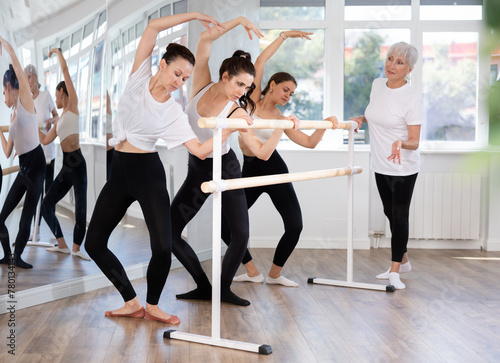 Elderly woman teacher corrects movements of female dancers in studio