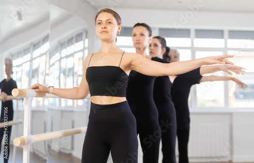 Elderly female teacher, along with students, participates in training, performs exercises, second position. Girls engaged in ballet studio, perform repetitions of elements and tasks