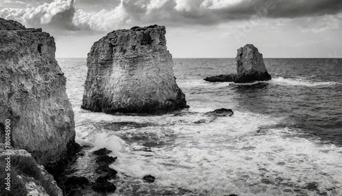 Vintage-style black and white seascape photo of a rocky shoreline with rough waves.
