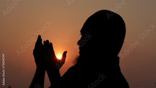 A Muslim old man praying with his hands raised to the sky in the afternoon twilight.