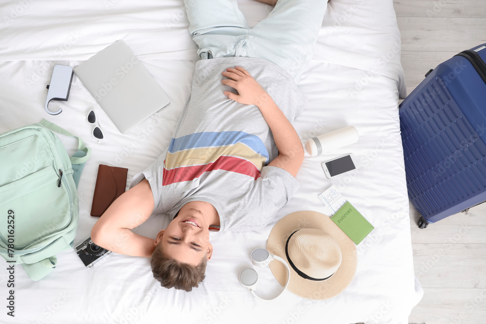 Fototapeta premium Male tourist with travel accessories lying on bed in hotel room, top view