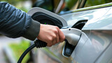 Close-up of a hand plugging in a charger into an electric vehicle at a charging station.