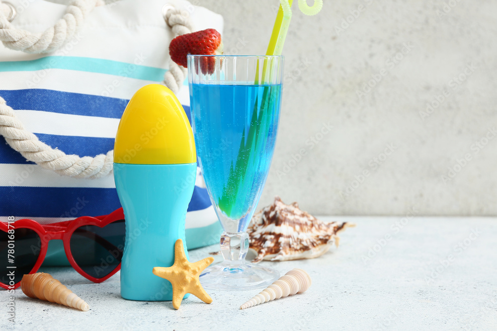 Bottle of sunscreen cream, glass of cocktail and beach accessories on white table near light wall