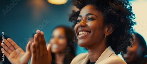A radiant woman with a happy expression claps her hands surrounded by a group of diverse individuals showing appreciation © LukaszDesign